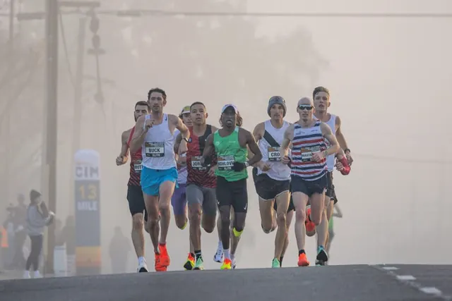 Lead pack of elite marathon runners racing through fog past the 13-mile marker